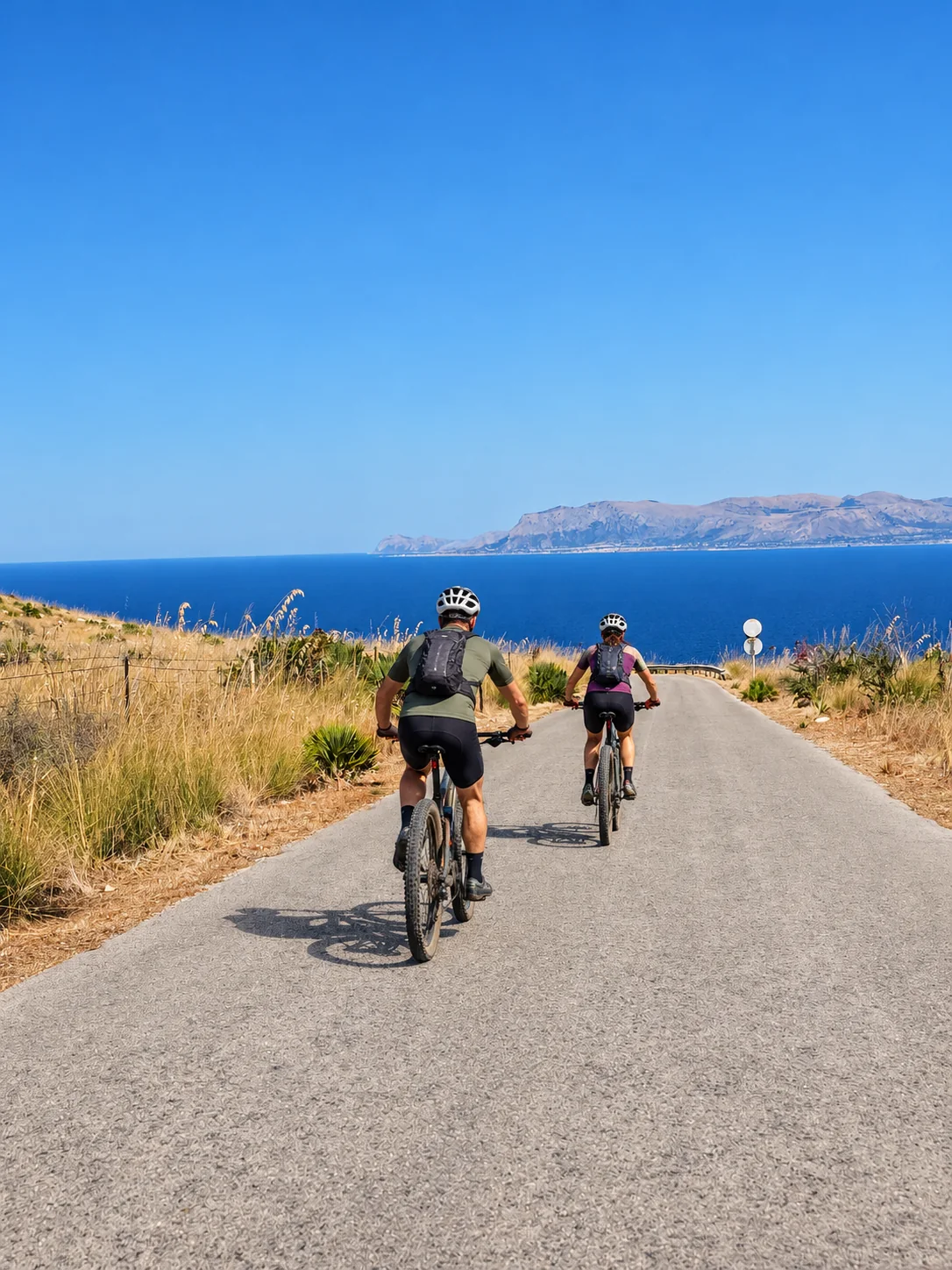 Due ciclisti su una strada panoramica verso il mare